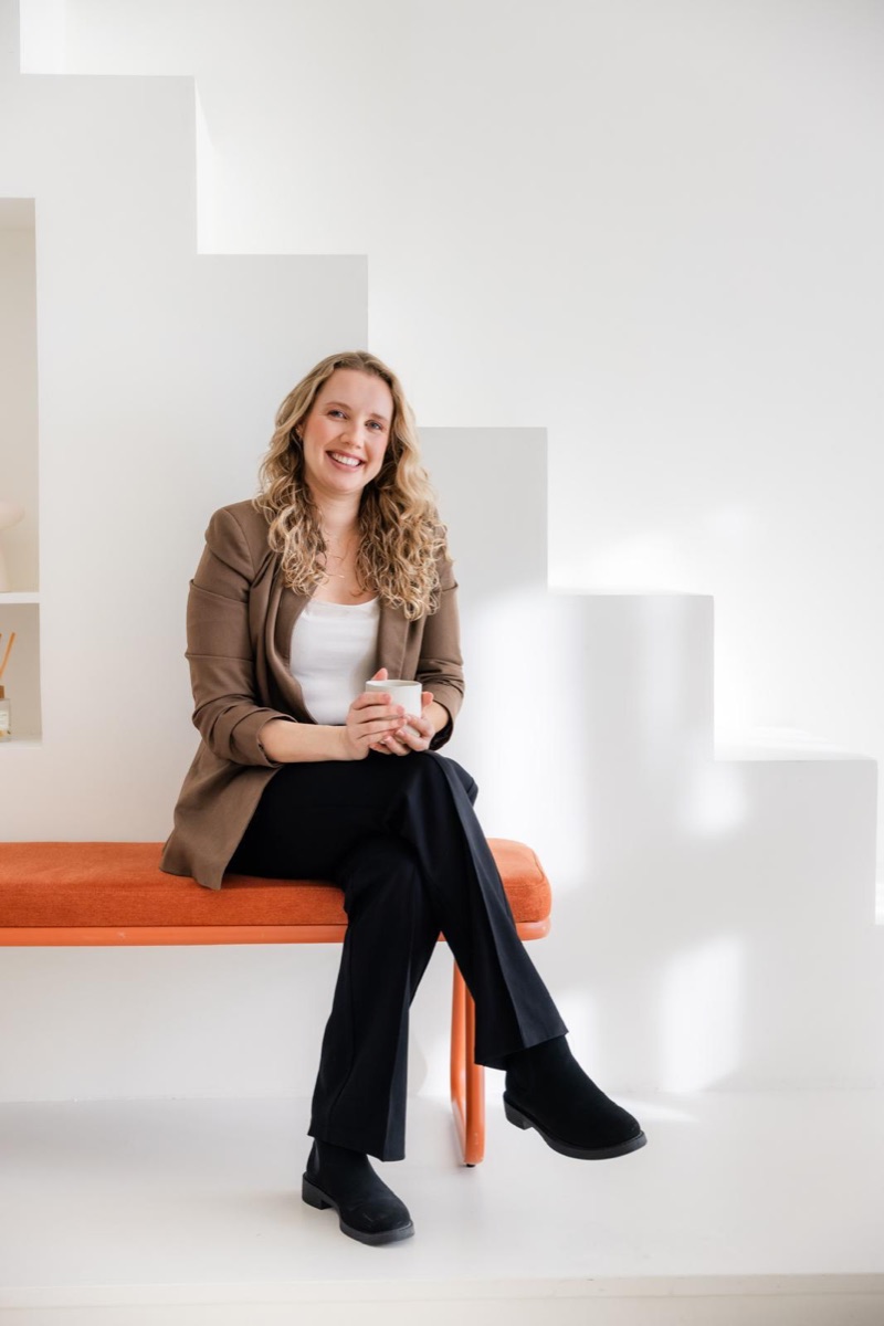 Debra Bekker op een oranje bankje met een kop koffie